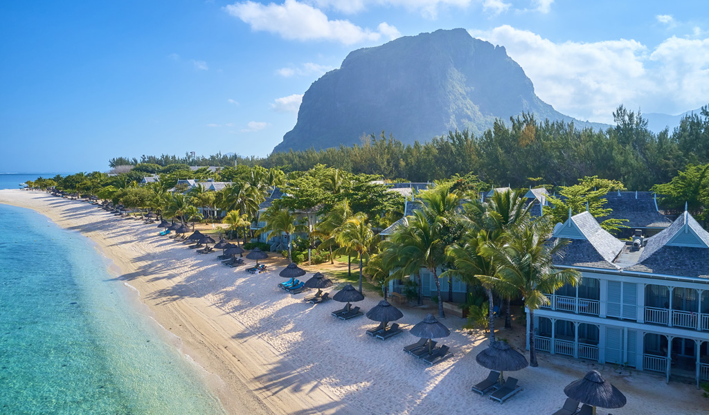Ein roter Leuchtturm steht auf einer grünen Düne an einem ruhigen Sandstrand