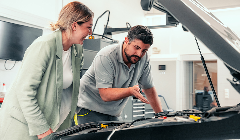 Eine Frau und ein Mann lächeln, während sie gemeinsam den Auto Motor inspizieren