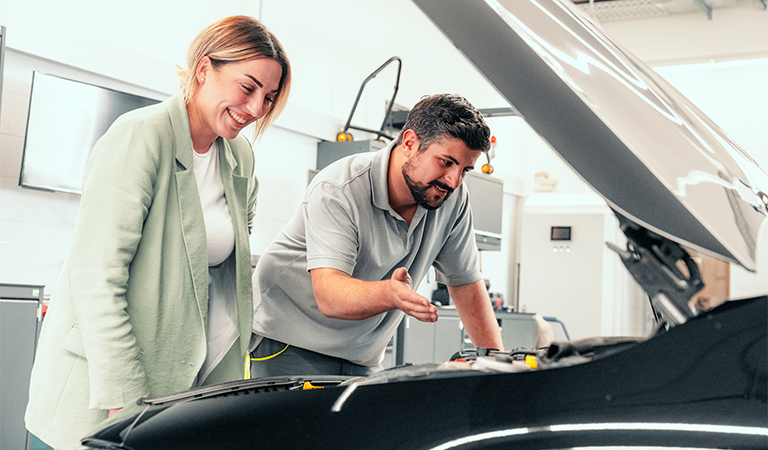 Eine Frau mit blonder Kurzhaarfrisur lächelt freundlich neben einem Mann am Auto