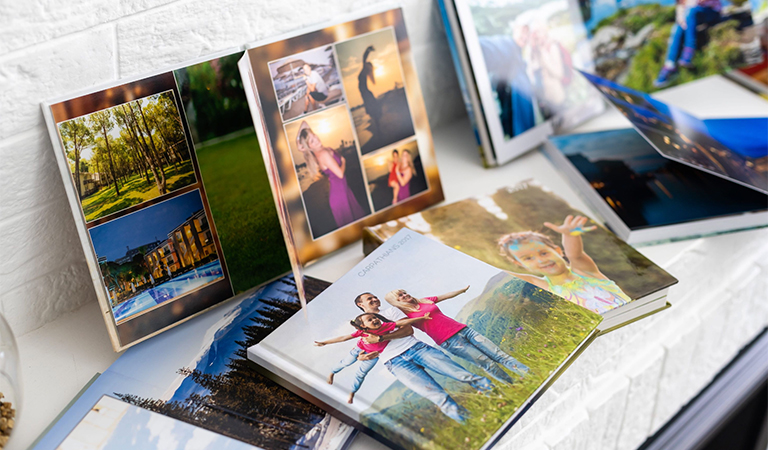 Mehrere Fotobücher zeigen fröhliche Menschen und bunte Naturaufnahmen auf weißem Tisch