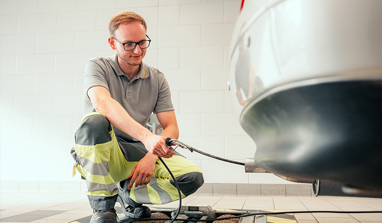 Ein junger Mann mit Brille und grauem Poloshirt lächelt und prüft das Auto-Abgas