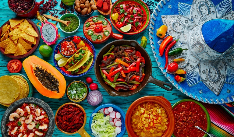 Bunte mexikanische Gerichte mit frischem Gemüse und Gewürzen, neben Sombrero