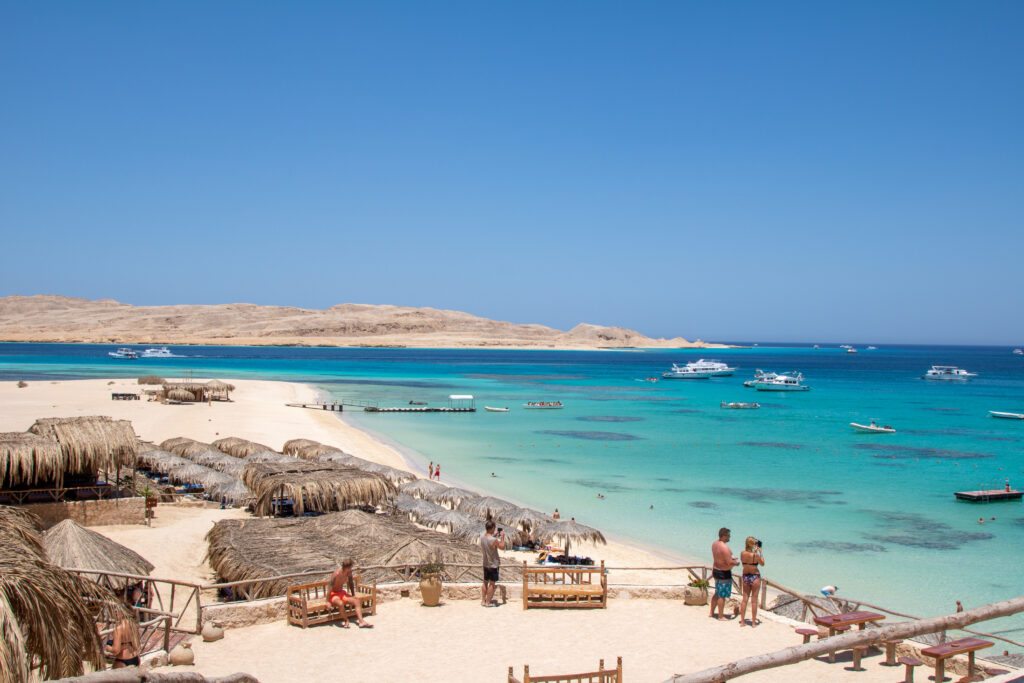 Mehrere Menschen geniessen entspannt das türkisfarbene Meer an einem sonnigen Sandstrand