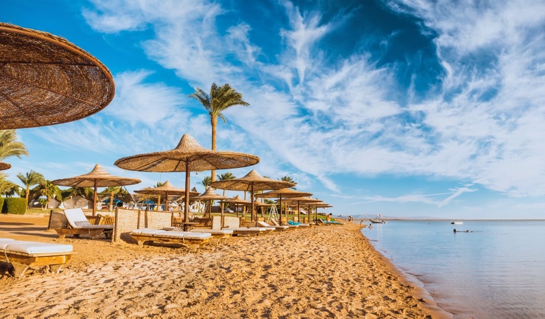 Ein leerer Sandstrand mit strohgedeckten Sonnenschirmen und blauem Himmel