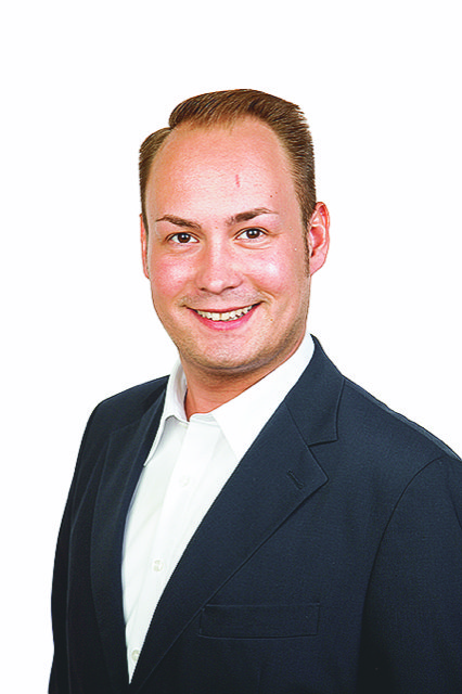 Ein Mann mit braunen Haaren trägt einen dunklen Anzug und weißes Hemd