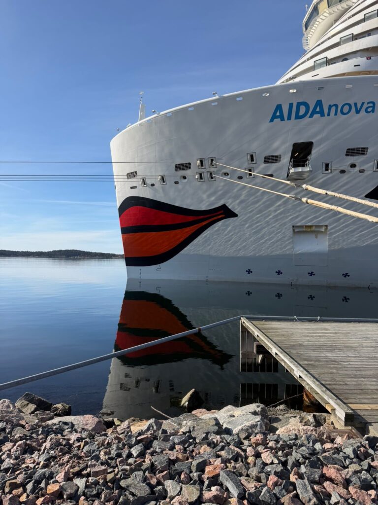 Das weiße Kreuzfahrtschiff AIDAnova liegt ruhig im klaren Wasser am Holzsteg