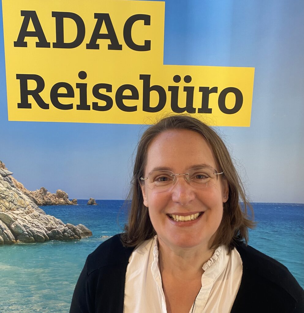 Frau mit brünettem Haar und neutralem Gesicht vor ADAC Reiseführer-Plakat