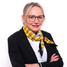 Eine Frau mit blondem Haar trägt einen gelben Schal und schwarzen Blazer