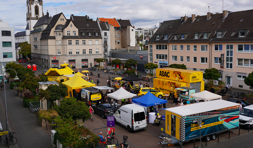 Eine belebte Straßenfestszene mit bunten ADAC Zelten und Menschen in fröhlicher Stimmung