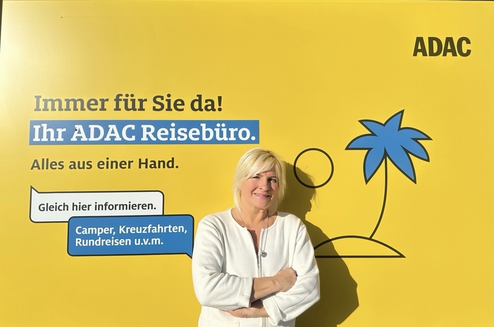Eine Frau mit blonden Haaren steht nachdenklich vor einer gelben ADAC-Wand
