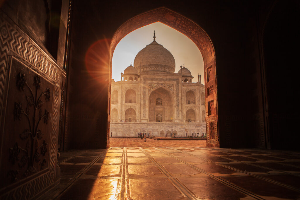 Die Sonne strahlt durch ein Tor auf das helle Taj Mahal im Hintergrund