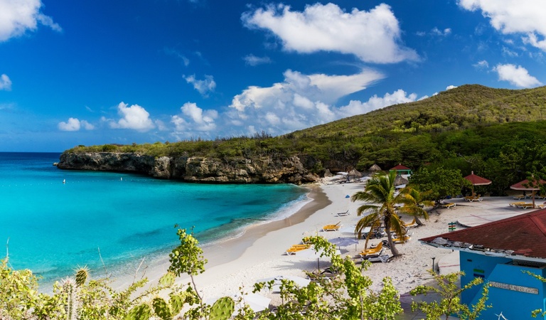 Ein tropischer Strand mit türkisfarbenem Wasser, grünen Hügeln und Palmen