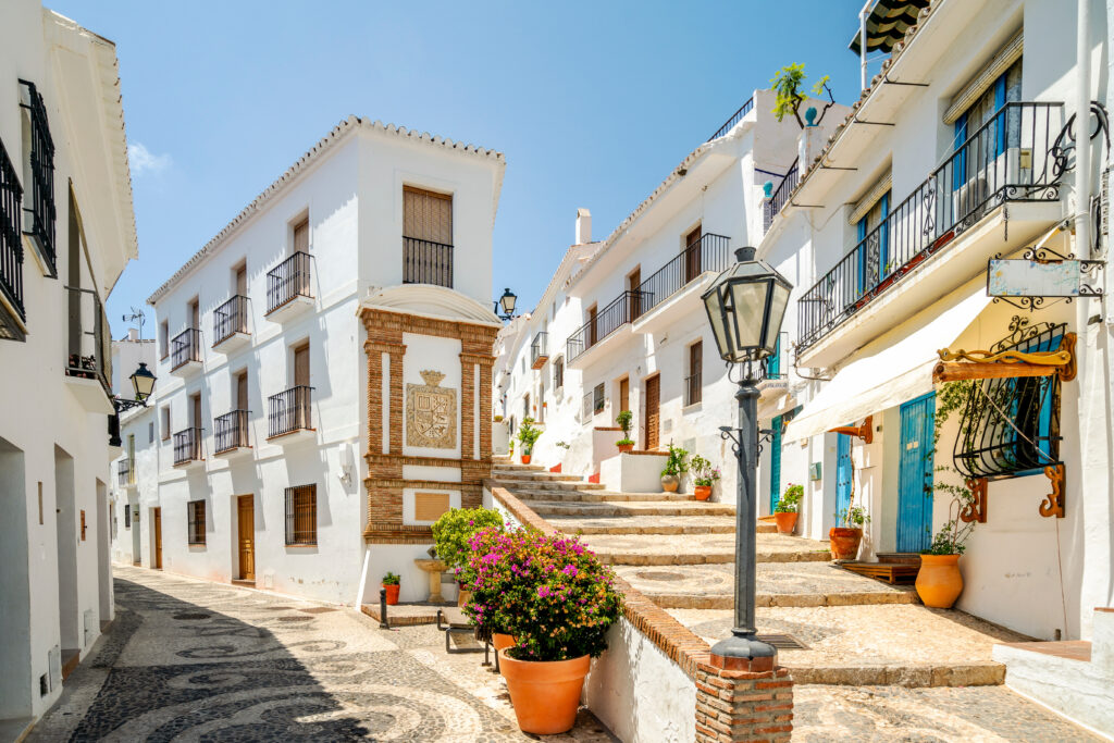 Eine sonnige spanische Gasse mit weißen Häusern, bunten Blumen und alten Laternen