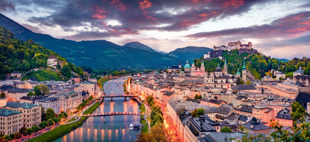 Panorama einer Stadt bei Sonnenuntergang mit Fluss, bunten Gebäuden und grünen Hügeln