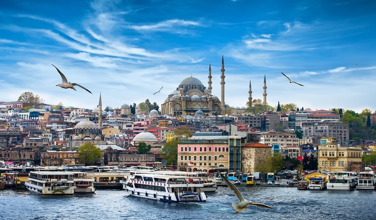 Boote fahren auf blauem Wasser vor einer bunten Stadt mit Moschee und fliegenden Möwen