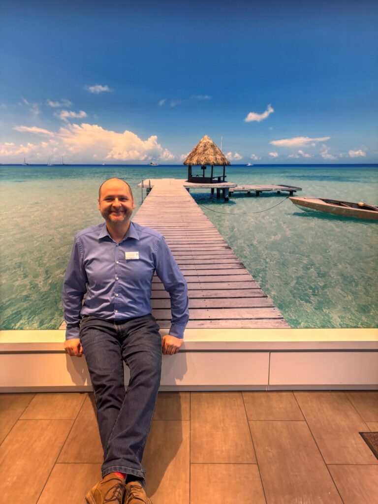 Eine Person mit blauem Hemd und Jeans sitzt entspannt vor einem Strandmotiv