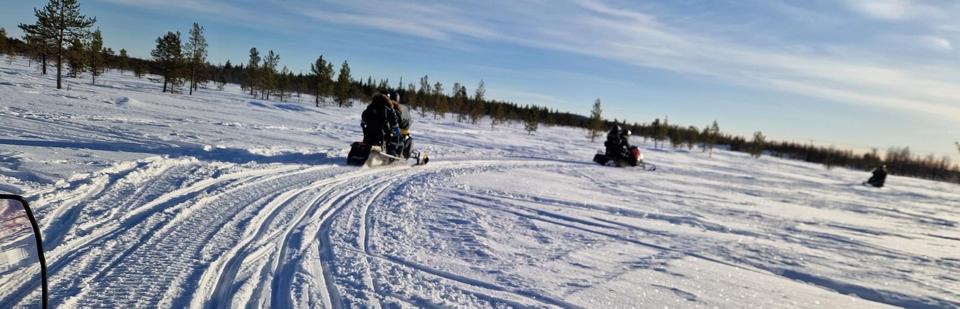Mehrere Personen fahren auf schwarzen Schneemobilen durch eine verschneite Landschaft