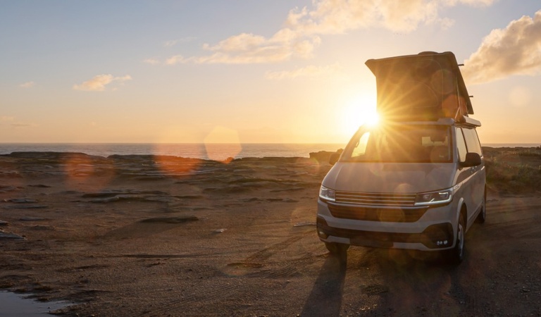 Ein silberner Camper steht bei Sonnenuntergang am Strand mit geöffnetem Dach