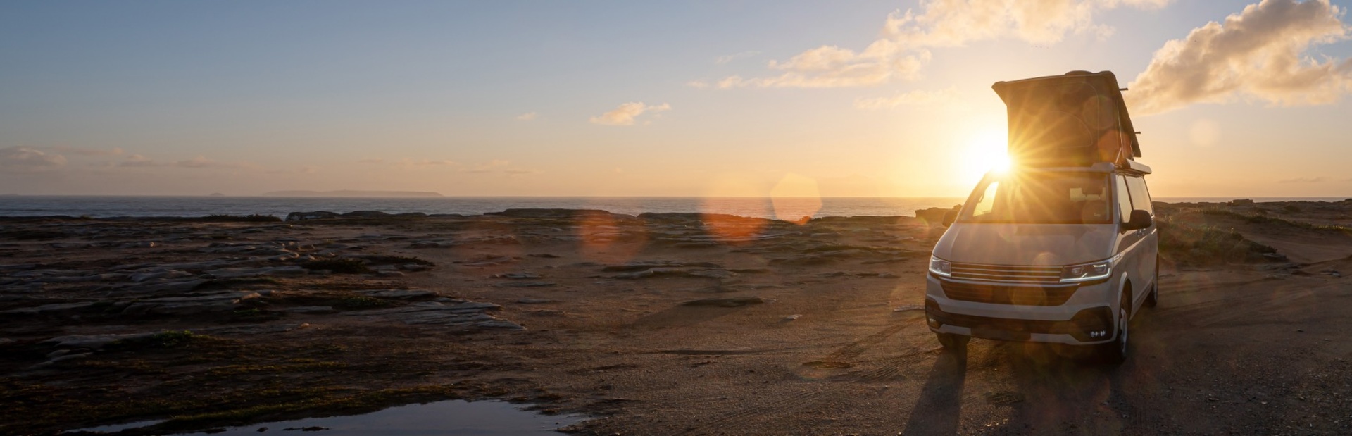 Ein weißer Van mit offenem Dach steht am sonnigen Meer, warme Lichtreflexe