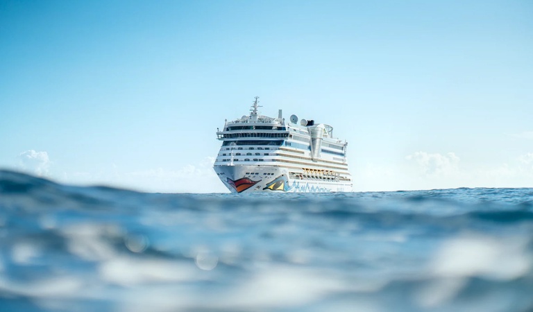 Ein großes weißes Kreuzfahrtschiff fährt bei klarem Himmel auf dem blauen Meer
