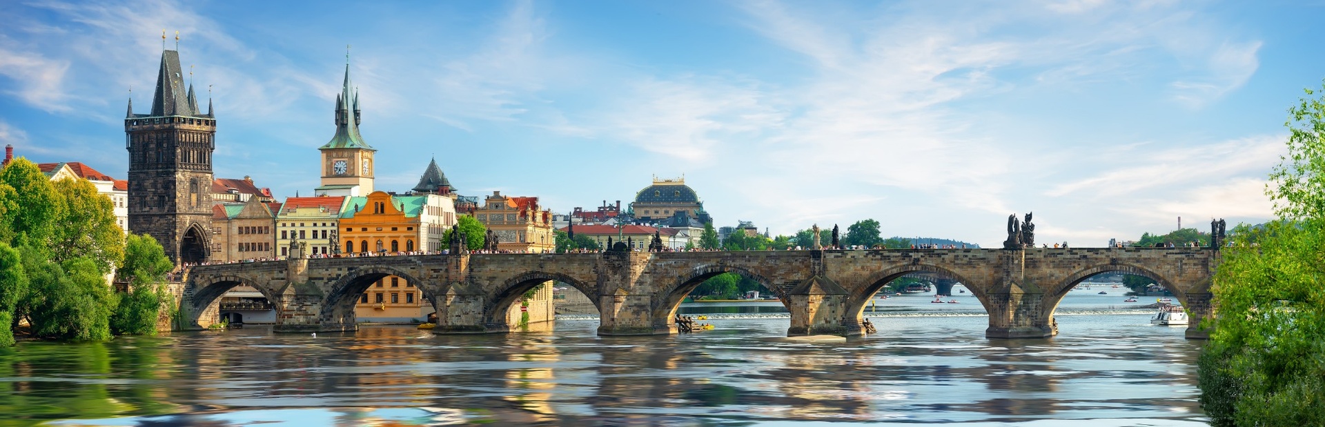 Eine alte Brücke mit historischen Statuen und bunten Gebäuden im Hintergrund