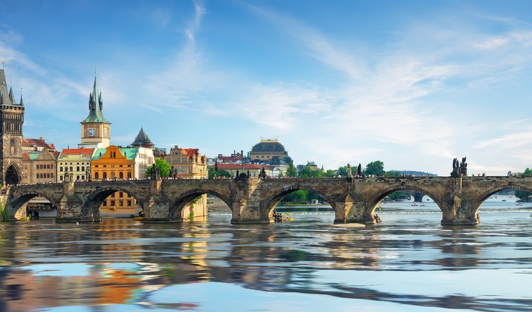 Die Karlsbrücke in Prag spiegelt sich im klaren Wasser vor bunten historischen Gebäuden