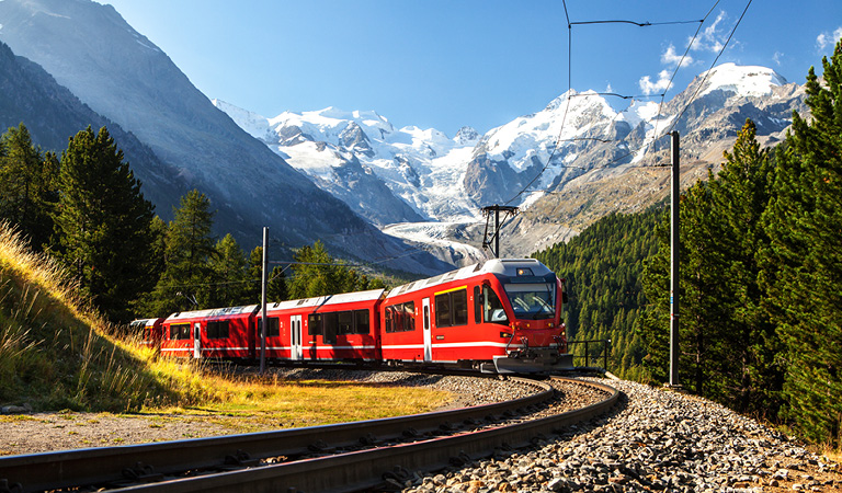 Grüne Wiesen mit gelbem Blütenteppich vor schneebedeckten Bergen und Bauernhäusern