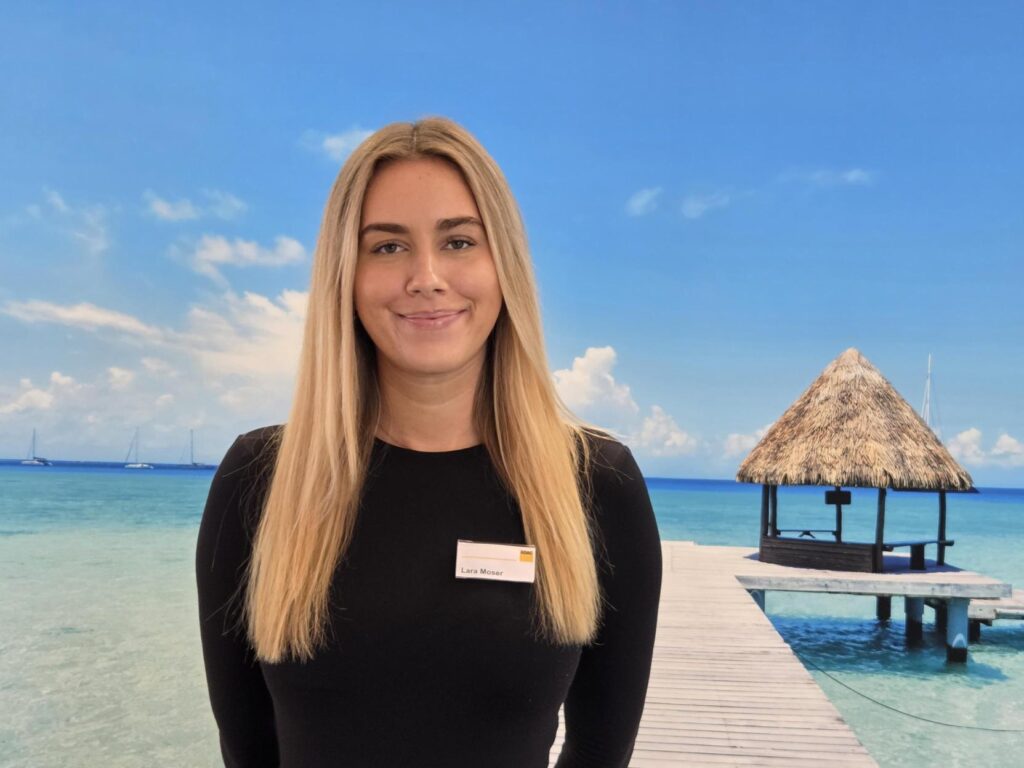 Junge Frau mit langen blonden Haaren und leichtem Lächeln vor einem Steg am Meer