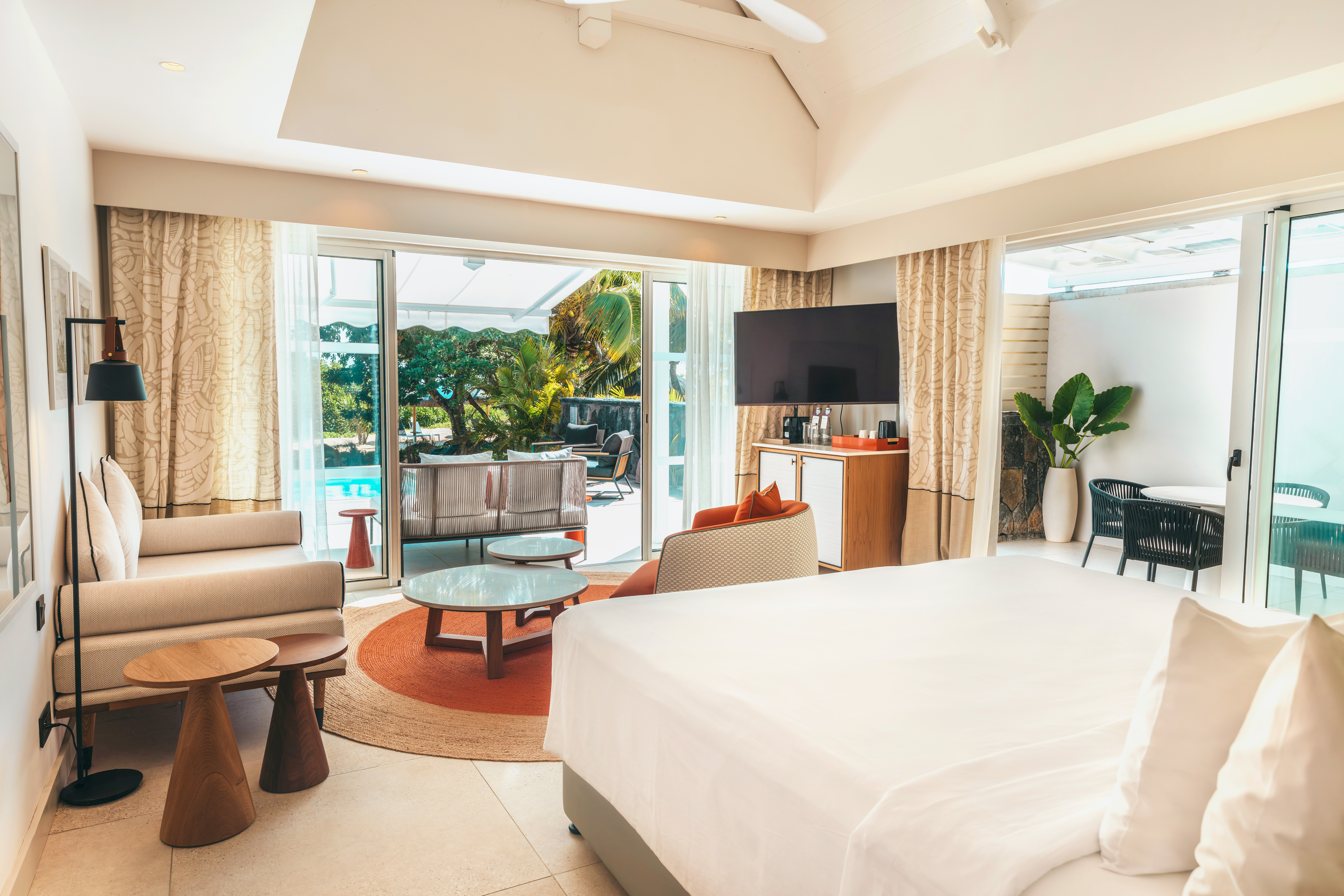 Geräumiges Zimmer mit weißem Bett, Sofas, Fernseher und Ausblick zum Pool