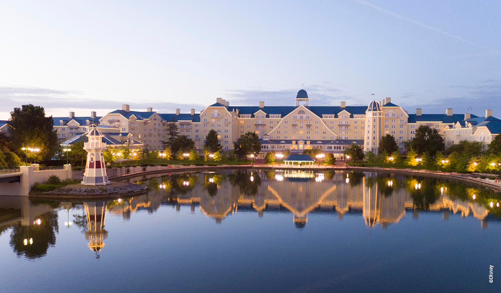Großes hellgelbes Hotel spiegelt sich ruhig im klaren See bei Sonnenuntergang