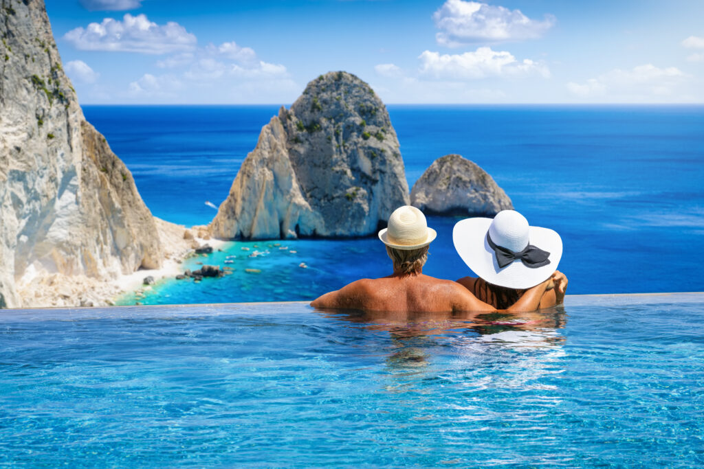Ein Paar mit hellen Hüten genießt entspannt den Blick auf türkisblaues Meer