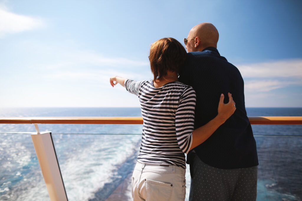 Zwei Menschen stehen umarmt auf einem Schiff und blicken lächelnd aufs Meer