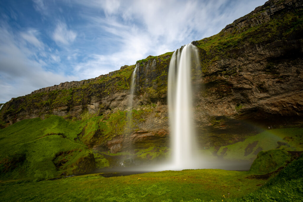 Ein mächtiger Wasserfall stürzt von einer grünen Klippe vor bewölktem Himmel