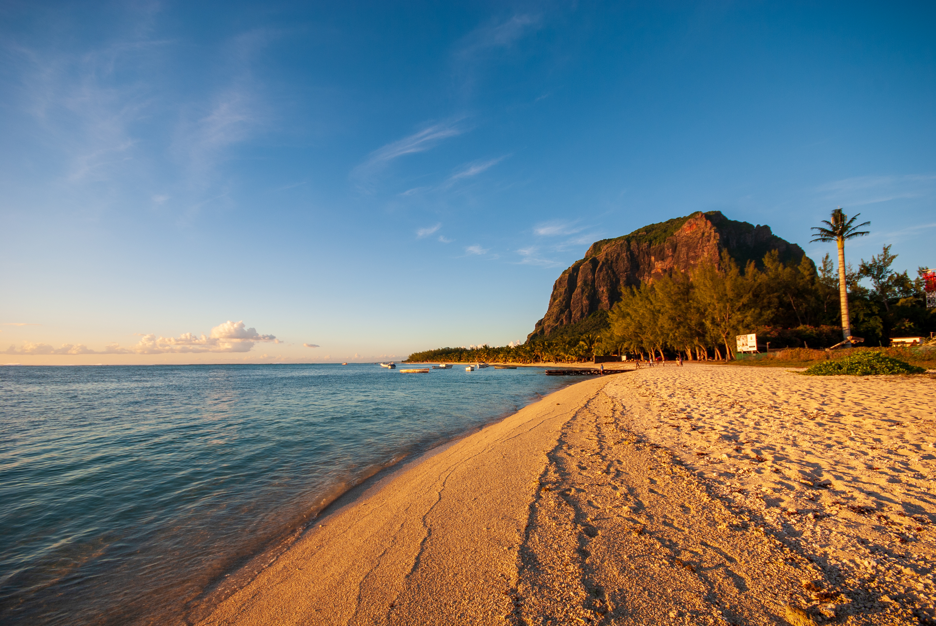 Ein Sandstrand mit türkisfarbenem Wasser und einem grünen Berg im Sonnenlicht