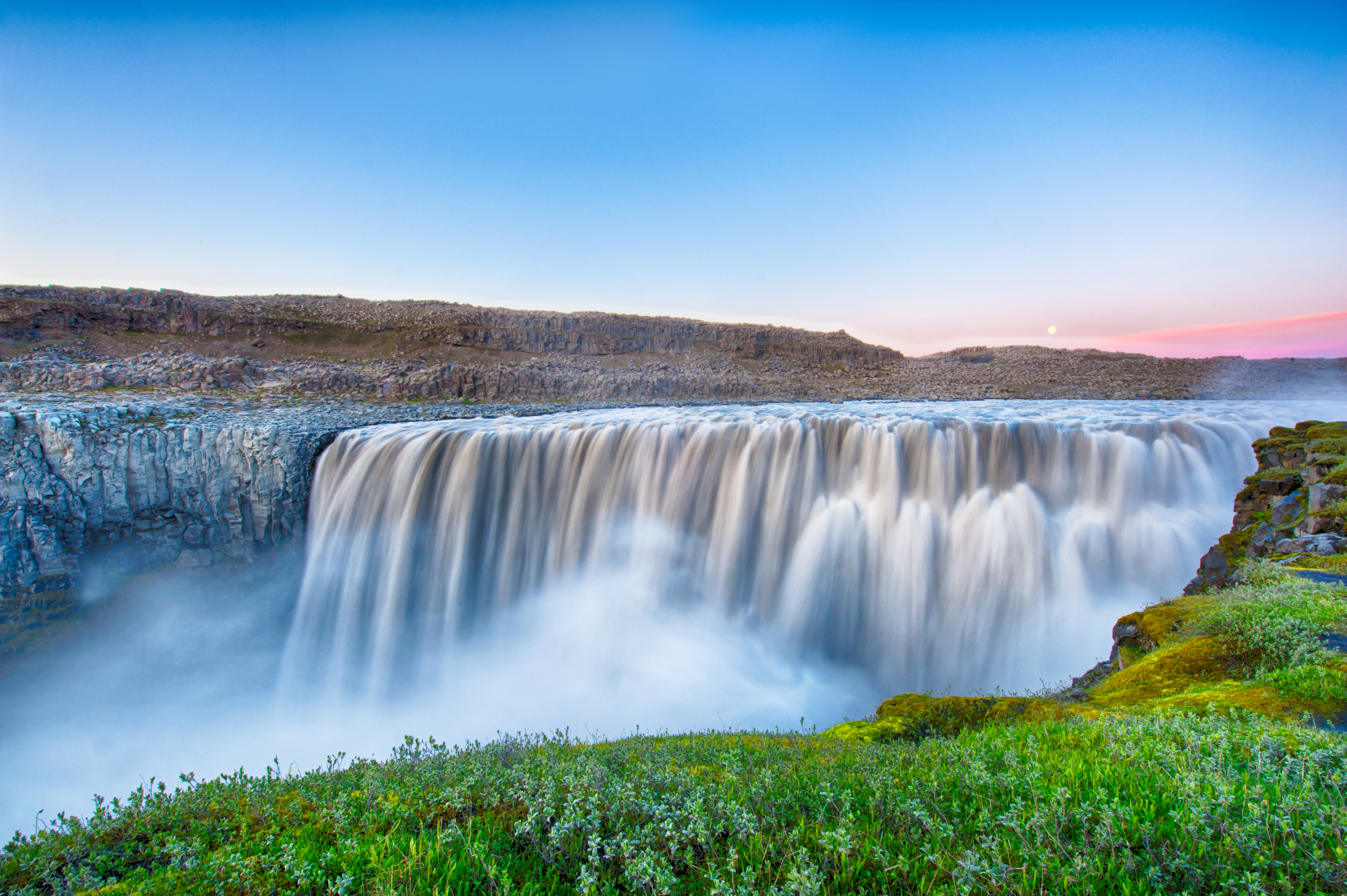 Ein breiter Wasserfall stürzt mit weißem Schaum in eine grüne Landschaft