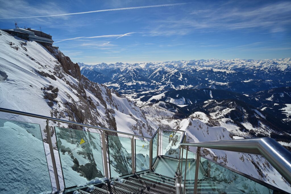 Schnee bedeckte Alpen mit Aussichtsterrasse, gläsernem Geländer und blauem Himmel