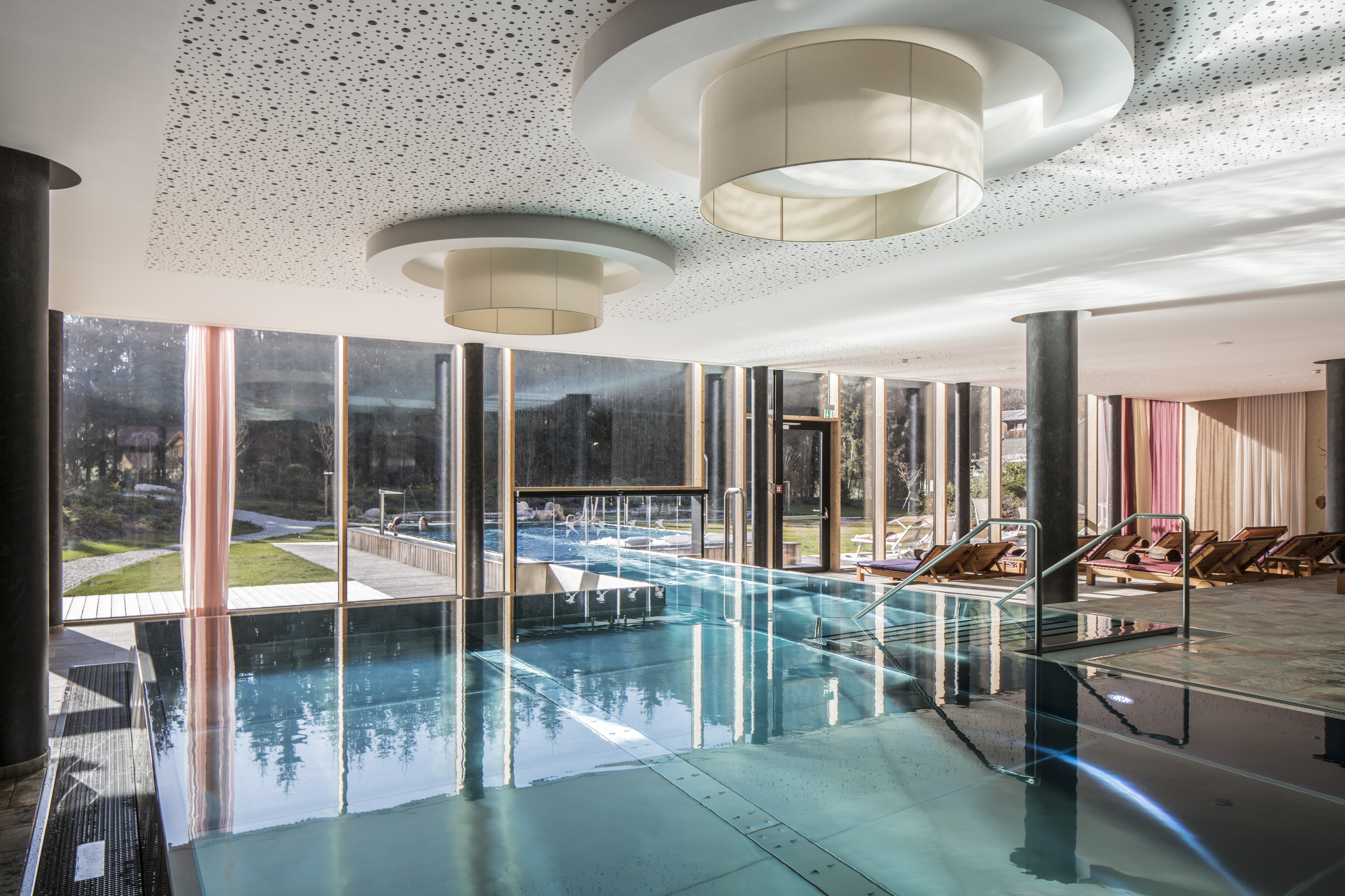 Ein eleganter Innenpool mit großen Fenstern, modernen Deckenlampen und stilvollen Liegen