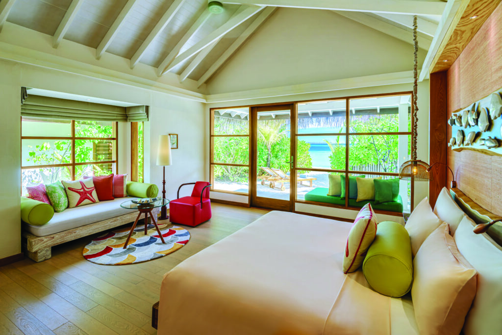 Helles Schlafzimmer mit großen Fenstern, buntem Teppich und Seeblick