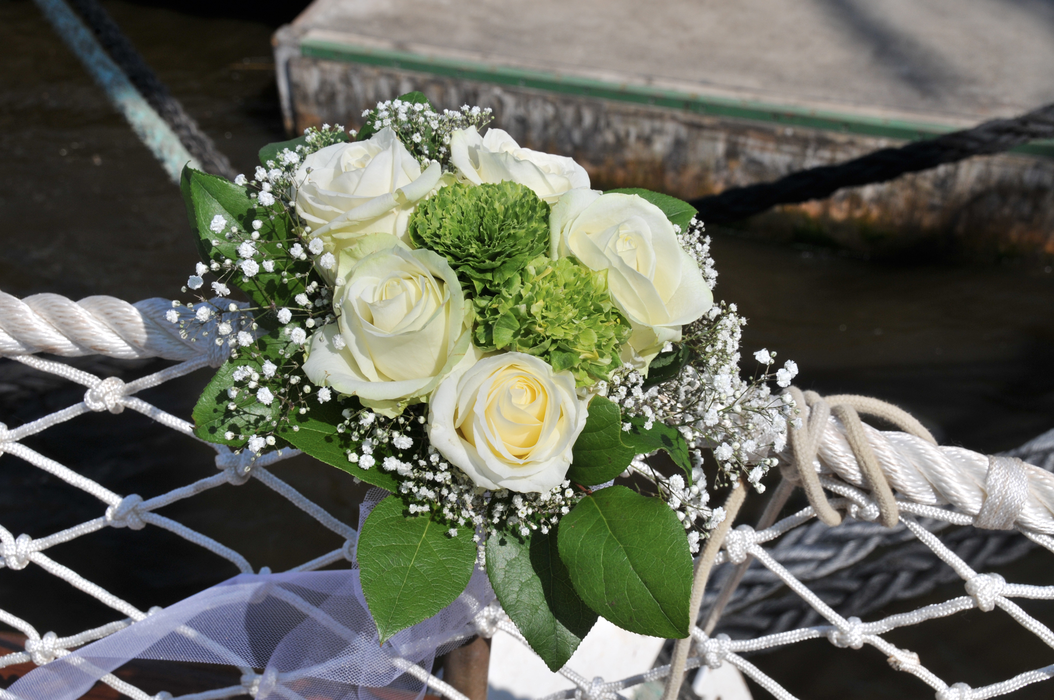 Ein Strauß weißer Rosen und grüner Blumen liegt dekorativ auf einem Knoten im Netz