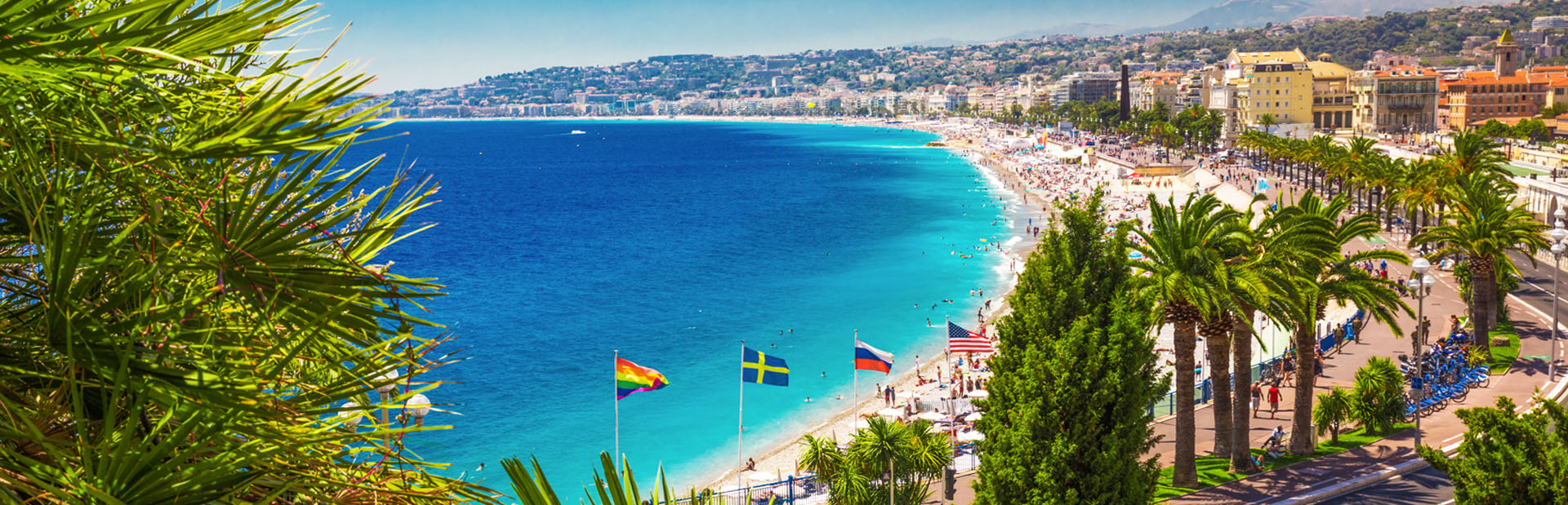 Strand mit türkisblauem Wasser, Palmen, bunte Fahnen und sonniger Himmel