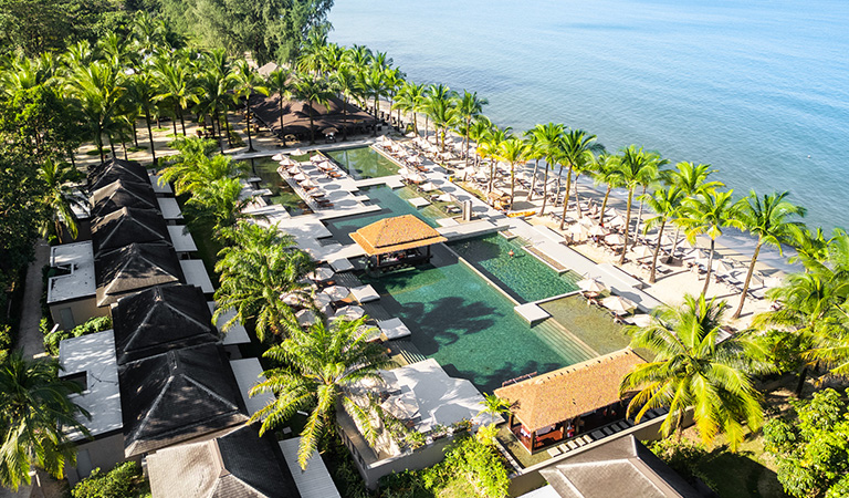 Elegante Resortanlage mit grünen Palmen und Pools direkt am ruhigen blauen Meer