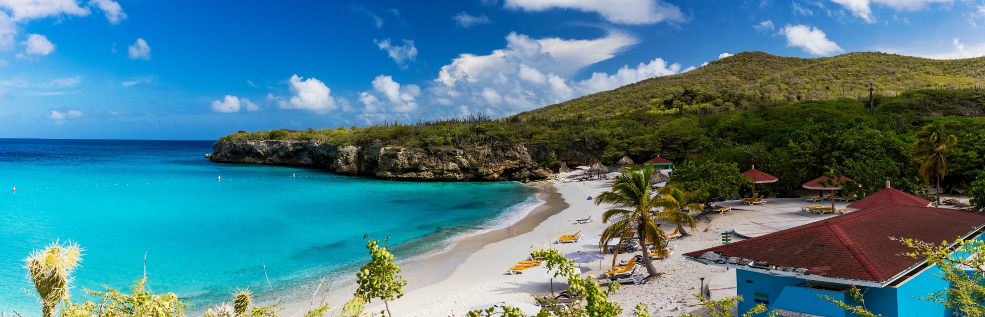 Ein tropischer Strand mit türkisblauem Wasser, Palmen und einem roten Haus