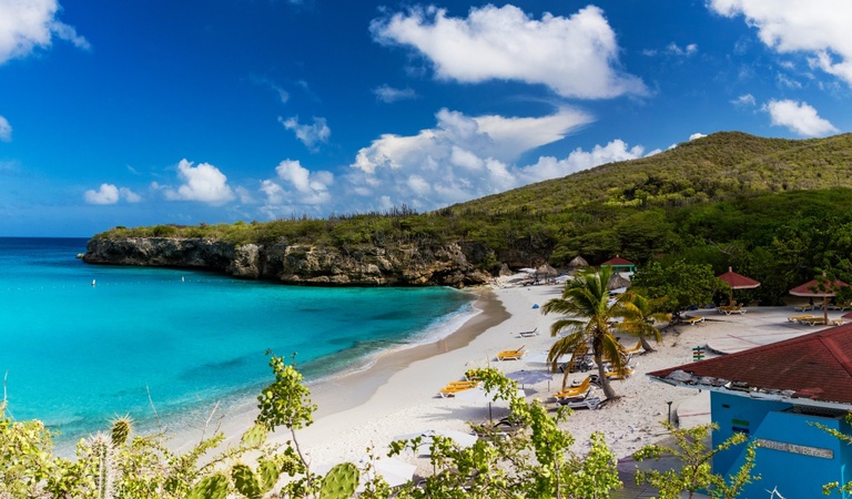 Idyllischer Strand mit türkisblauem Wasser, weißen Sand und grünen Palmen