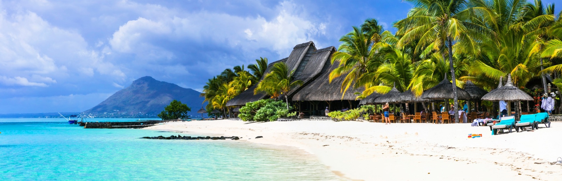 Ein tropischer Strand mit türkisfarbenem Wasser, Palmen und Strohhütten, Sonne strahlt