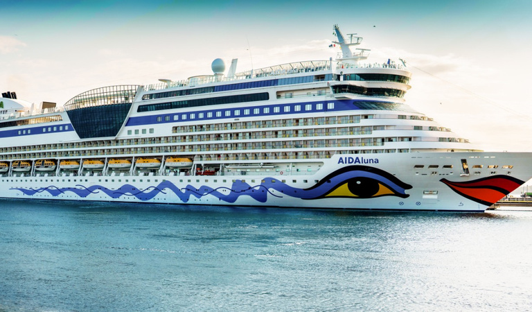 Ein weiß-blaues Kreuzfahrtschiff mit buntem Wellenmuster liegt im Hafen