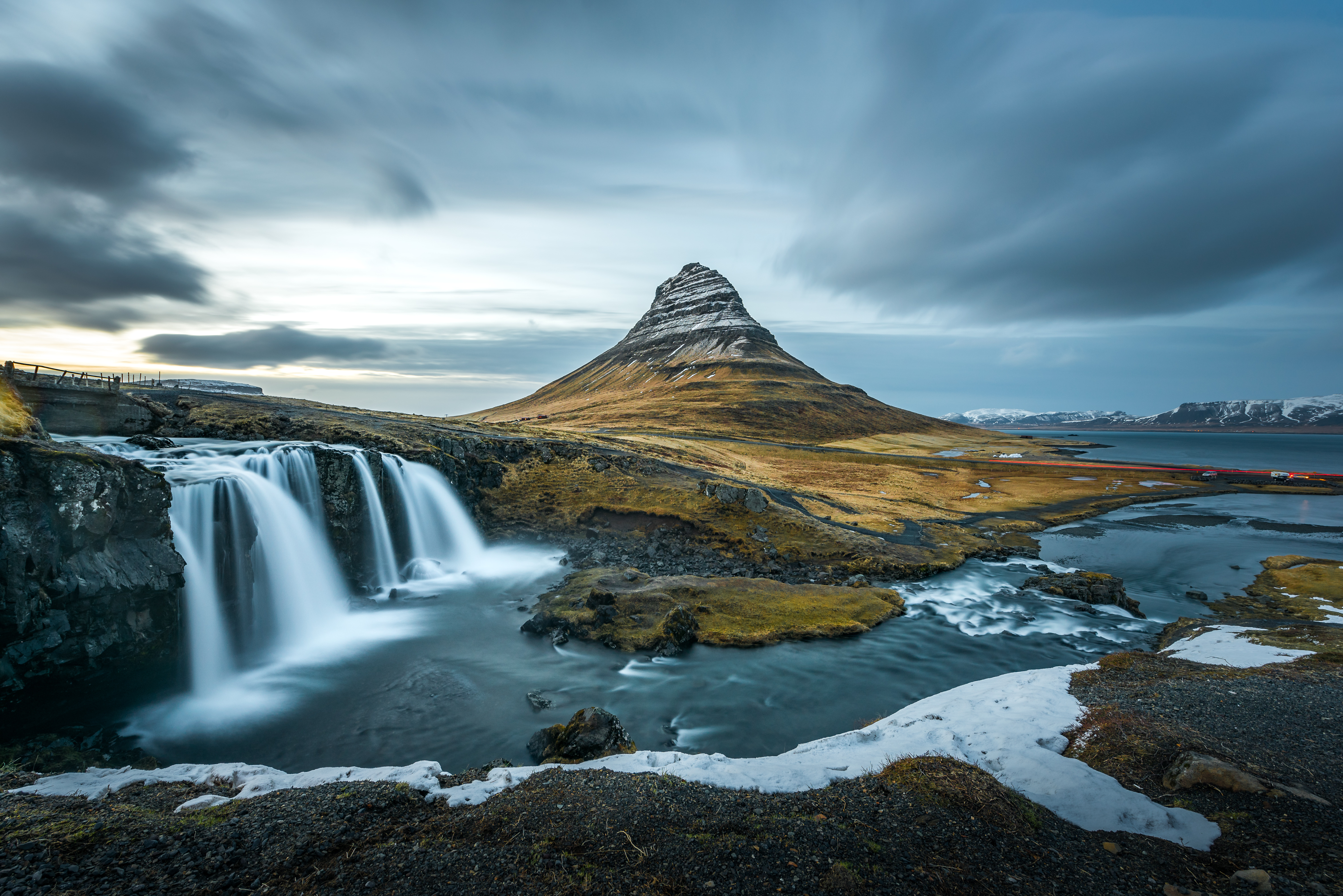 Ein ruhiger Wasserfall vor einem markanten Berg mit wolkenverhangenem Himmel