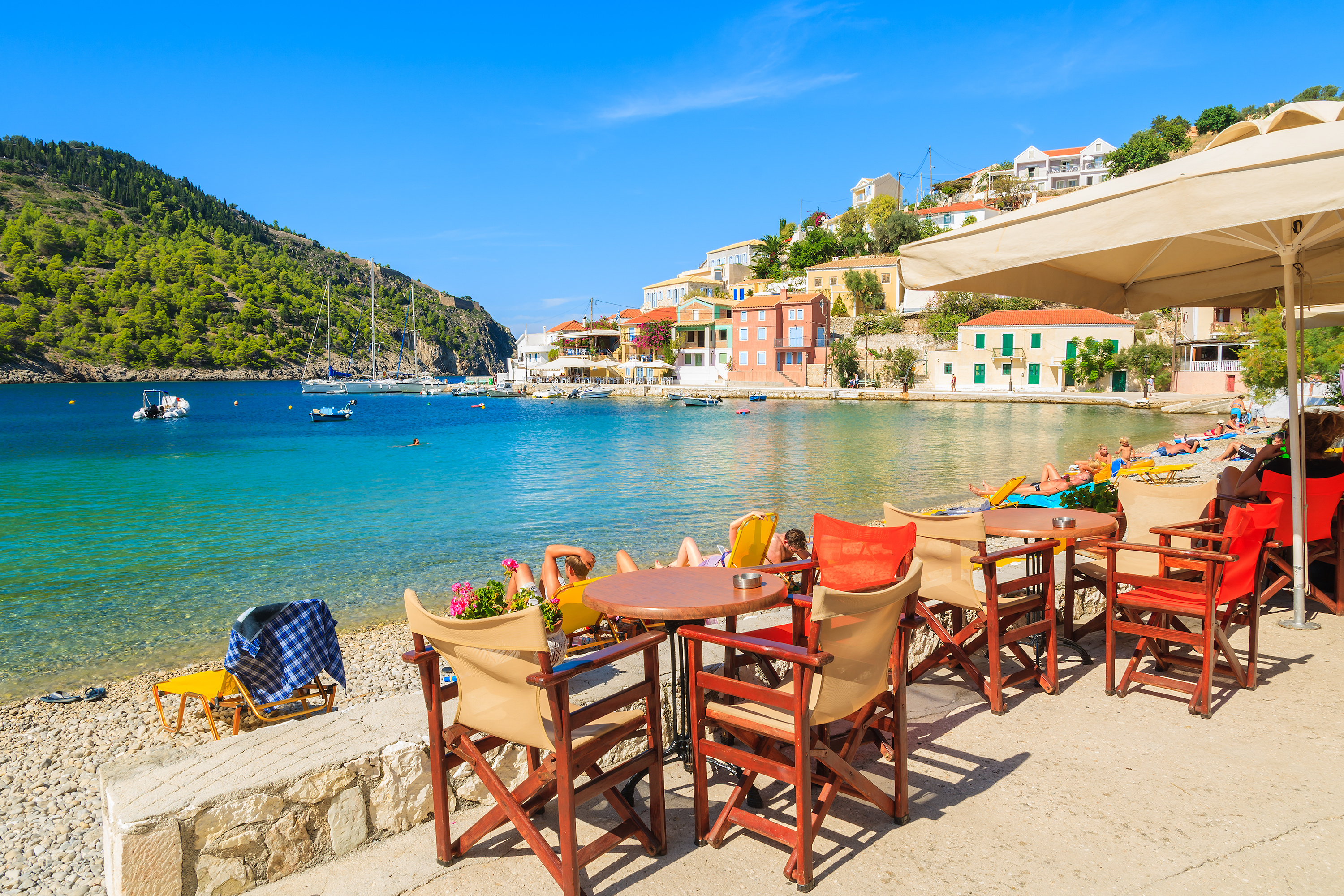 Bunte Tische und Stühle am sonnigen Strand mit klarem Wasser und grünen Hügeln