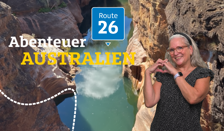 Eine lächelnde ältere Frau mit grauen Haaren formt ein Herz vor einer australischen Schlucht